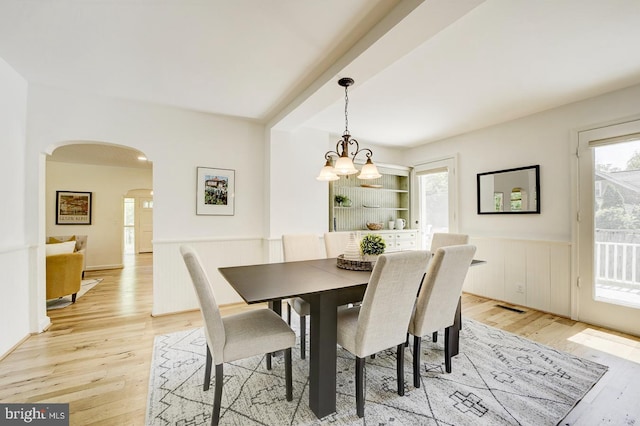 dining room with visible vents, arched walkways, a wainscoted wall, light wood finished floors, and a chandelier