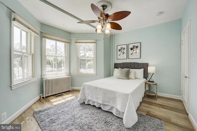 bedroom with radiator heating unit, baseboards, a ceiling fan, and light wood-type flooring