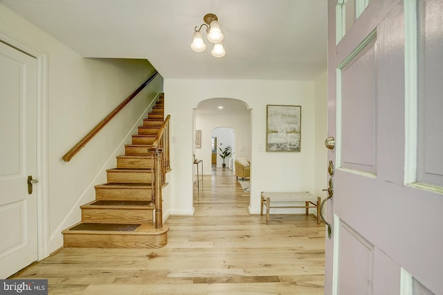foyer with arched walkways, stairs, and light wood-style flooring