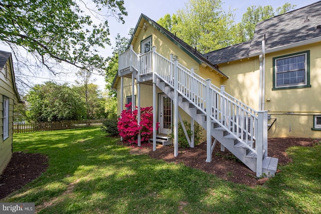 view of side of property with a lawn, stairway, fence, a shingled roof, and stucco siding