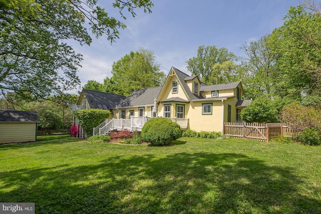 rear view of property featuring fence, a wooden deck, stucco siding, an outdoor structure, and a yard
