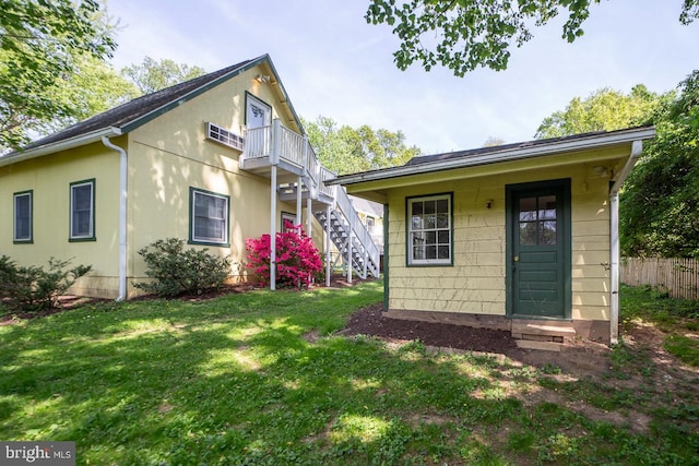 rear view of house featuring fence, stairs, stucco siding, a balcony, and a lawn