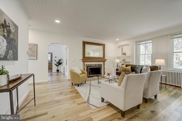 living area featuring a fireplace, arched walkways, radiator, recessed lighting, and light wood-type flooring