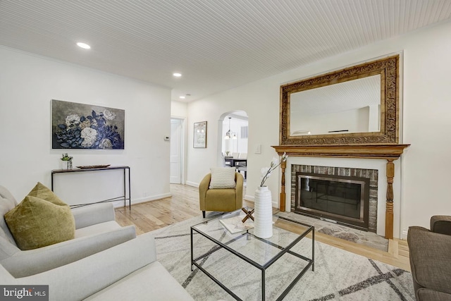 living area featuring a brick fireplace, arched walkways, recessed lighting, baseboards, and wood finished floors