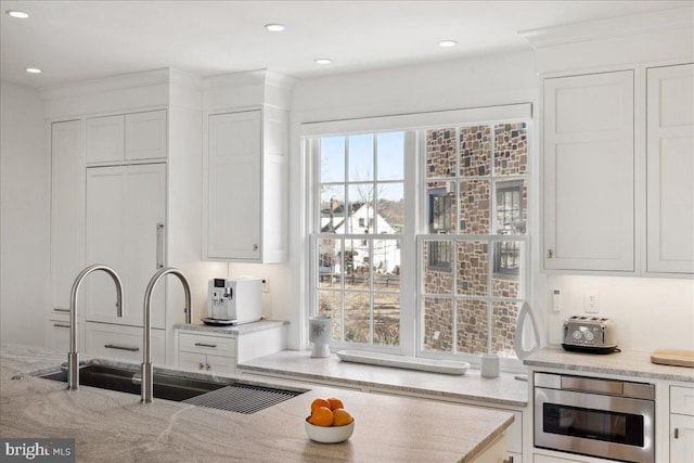 kitchen featuring light stone countertops, white cabinetry, and a sink