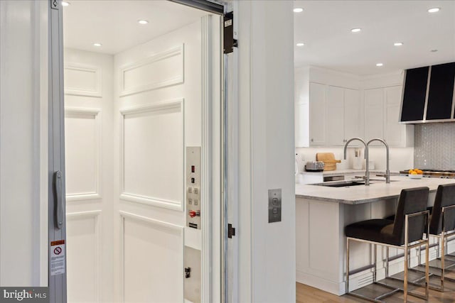 kitchen with light wood-type flooring, a sink, light stone counters, recessed lighting, and white cabinets