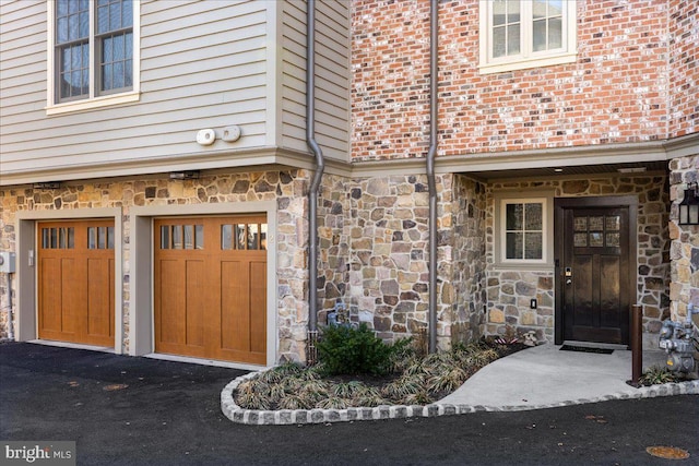 doorway to property featuring aphalt driveway, stone siding, and a garage