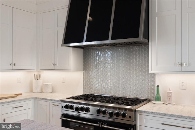 kitchen with light stone countertops, double oven range, white cabinets, exhaust hood, and backsplash