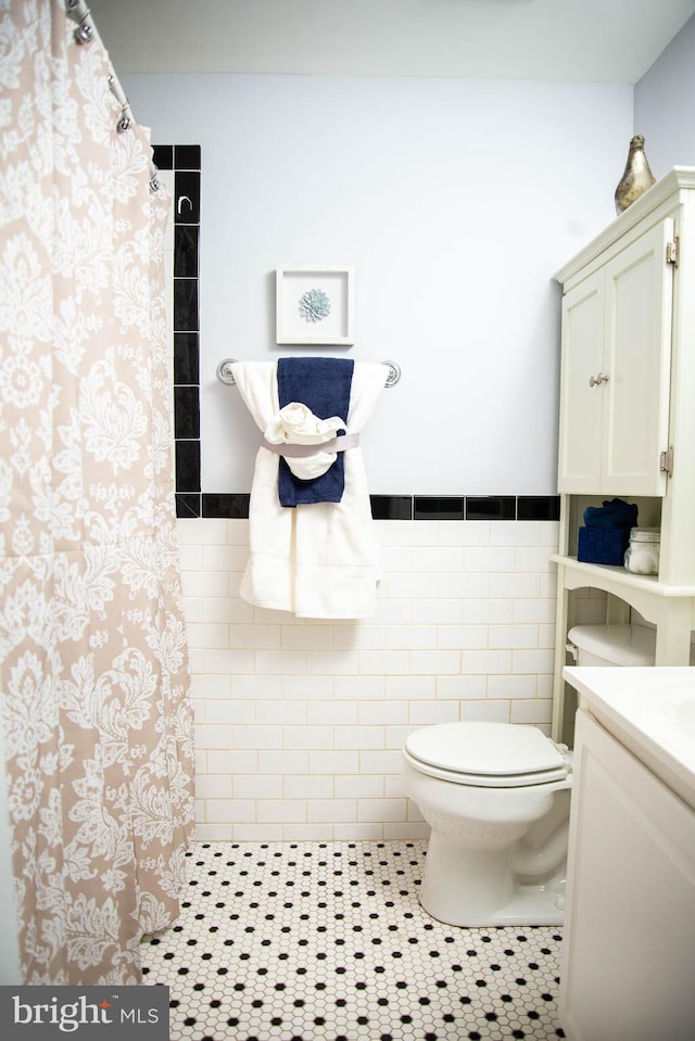 full bathroom with toilet, tile walls, wainscoting, a tile shower, and tile patterned floors