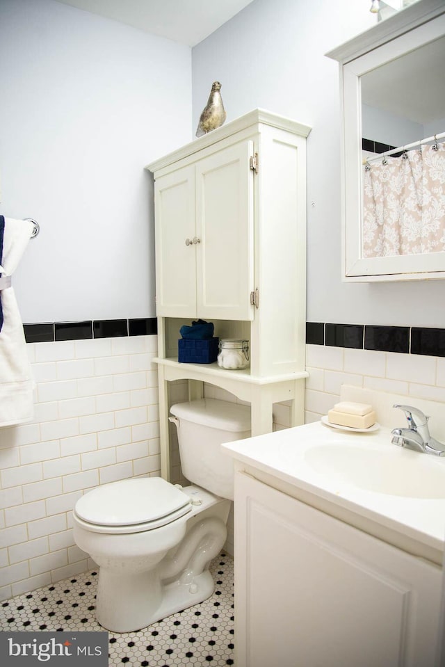 full bath featuring a wainscoted wall, tile walls, toilet, vanity, and tile patterned floors