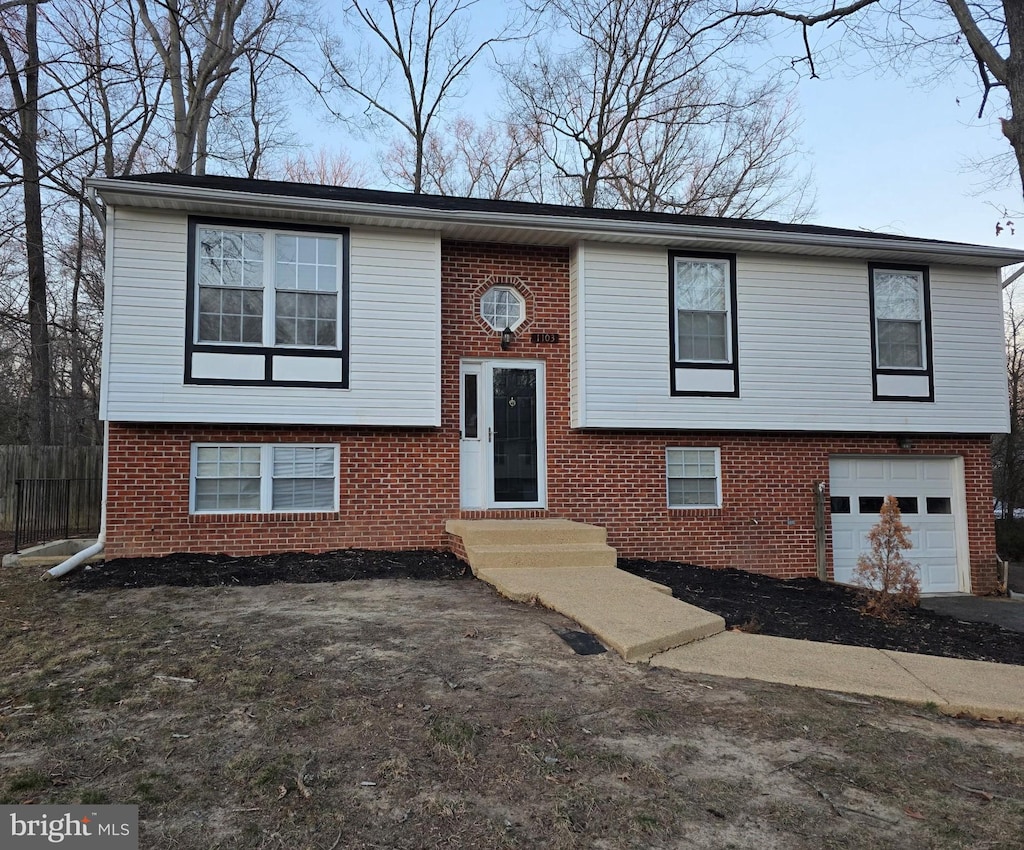 raised ranch with entry steps, brick siding, an attached garage, and fence