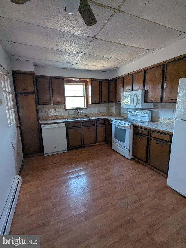 kitchen with tasteful backsplash, baseboard heating, a sink, wood finished floors, and white appliances