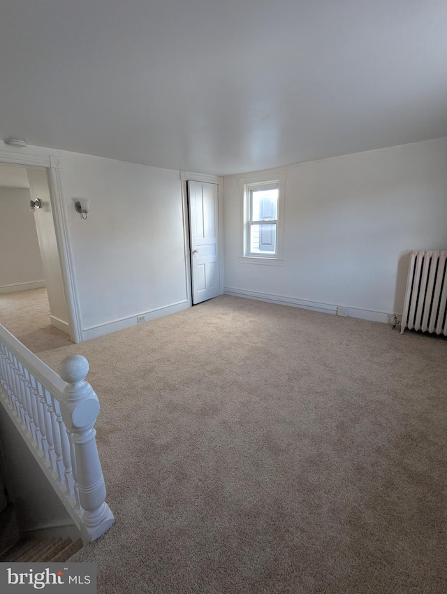 empty room featuring radiator, light carpet, stairway, and baseboards