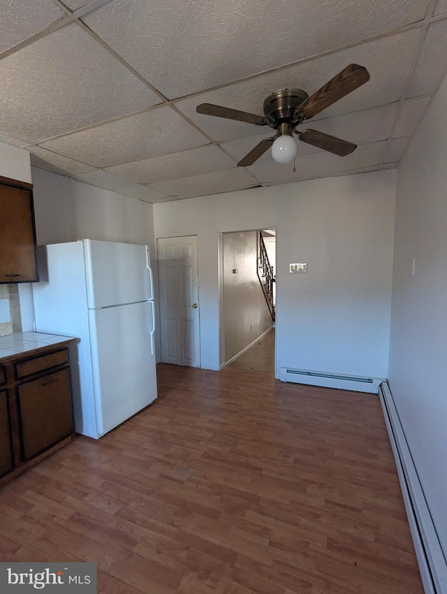 kitchen with tile countertops, wood finished floors, freestanding refrigerator, a paneled ceiling, and a baseboard heating unit