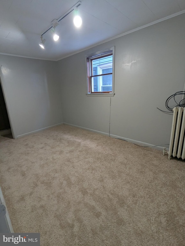 carpeted spare room featuring radiator, track lighting, baseboards, and crown molding