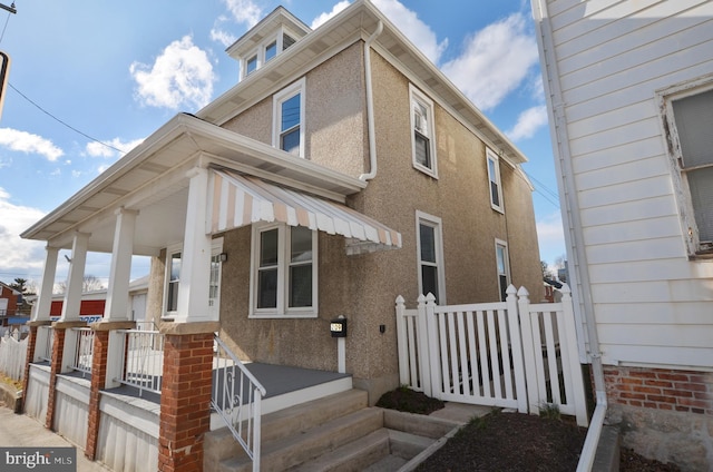 view of front facade with covered porch, fence, and stucco siding