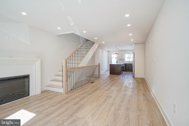 unfurnished living room featuring light wood-style floors, a glass covered fireplace, stairway, and recessed lighting