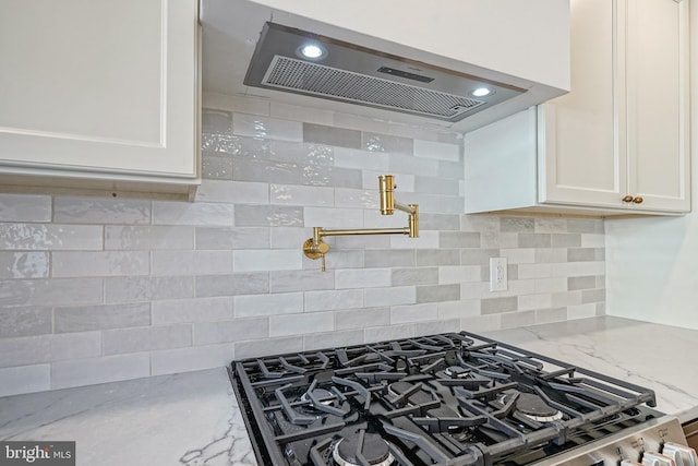 kitchen with light stone counters, tasteful backsplash, white cabinets, stainless steel gas stove, and extractor fan