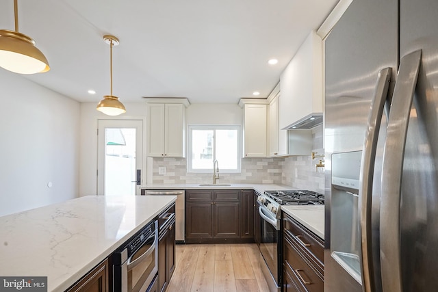 kitchen with light stone counters, appliances with stainless steel finishes, a sink, light wood-type flooring, and backsplash