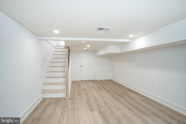 finished below grade area featuring light wood-style flooring, stairway, visible vents, and baseboards