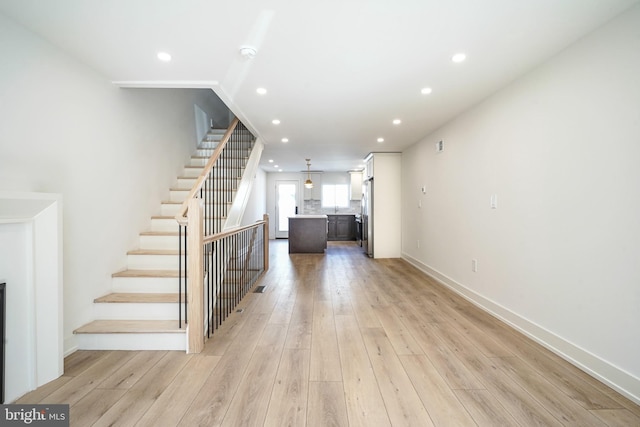 unfurnished living room with stairway, recessed lighting, light wood-style flooring, and baseboards