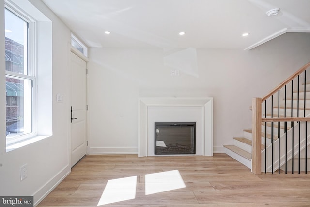 unfurnished living room with stairs, a wealth of natural light, a glass covered fireplace, and wood finished floors