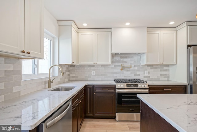 kitchen featuring white cabinets, decorative backsplash, custom range hood, appliances with stainless steel finishes, and a sink