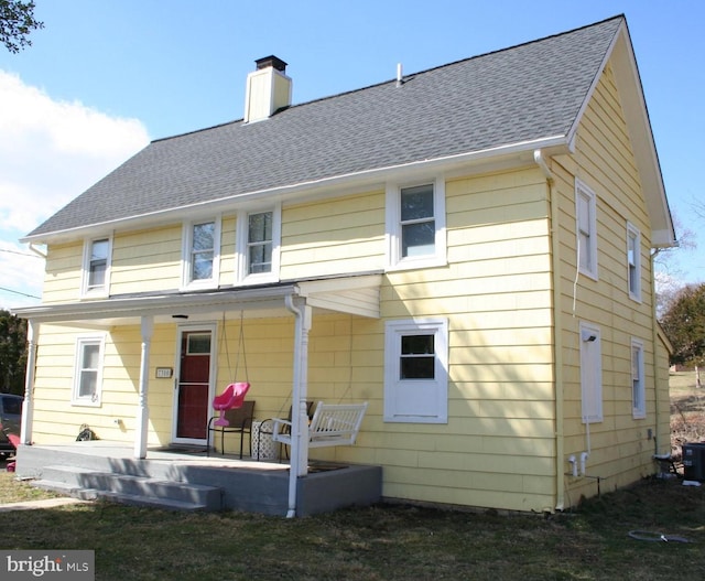 back of property with covered porch, a shingled roof, and a chimney