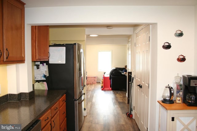 kitchen featuring dark stone counters, wood finished floors, freestanding refrigerator, and brown cabinets