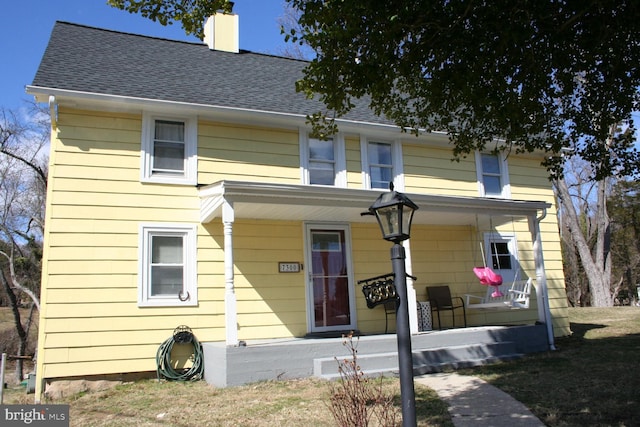 view of front of home with covered porch, roof with shingles, and a chimney