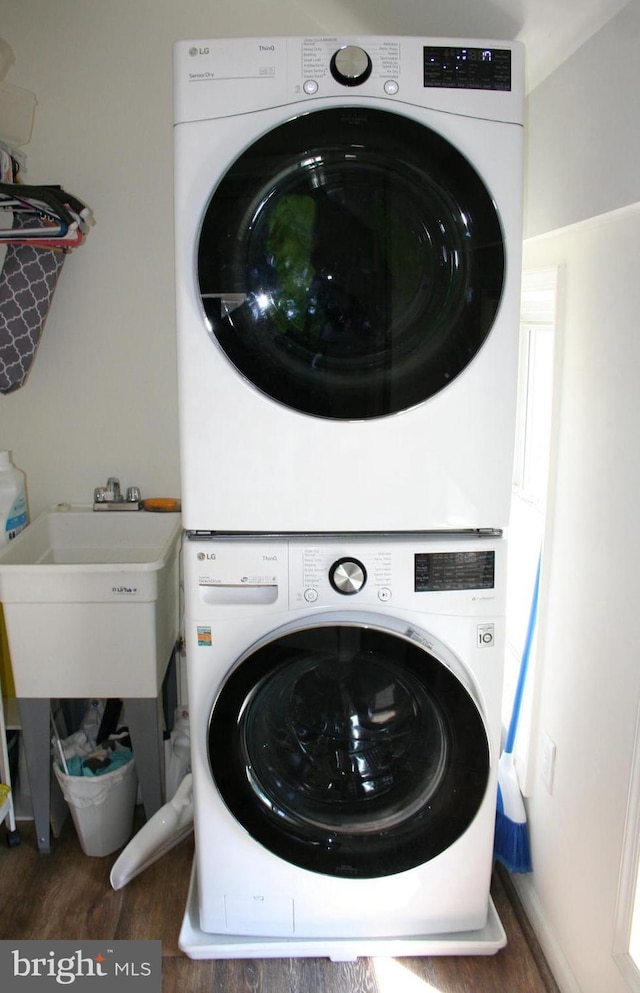 clothes washing area featuring laundry area, a sink, stacked washing maching and dryer, and wood finished floors