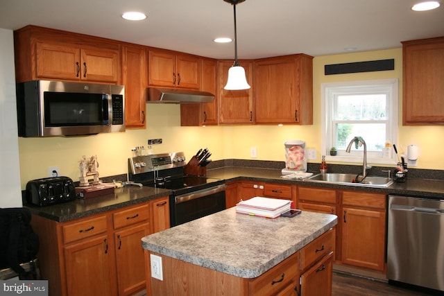 kitchen featuring appliances with stainless steel finishes, brown cabinets, under cabinet range hood, a sink, and recessed lighting