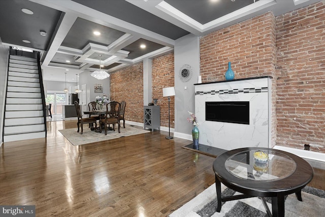 living area featuring brick wall, coffered ceiling, wood finished floors, baseboards, and stairway