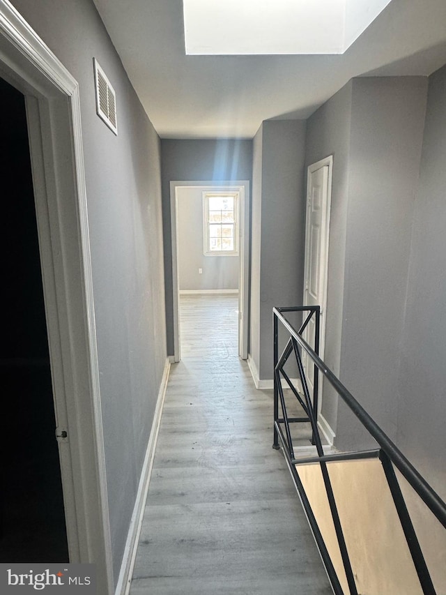 hallway featuring visible vents, wood finished floors, an upstairs landing, and baseboards