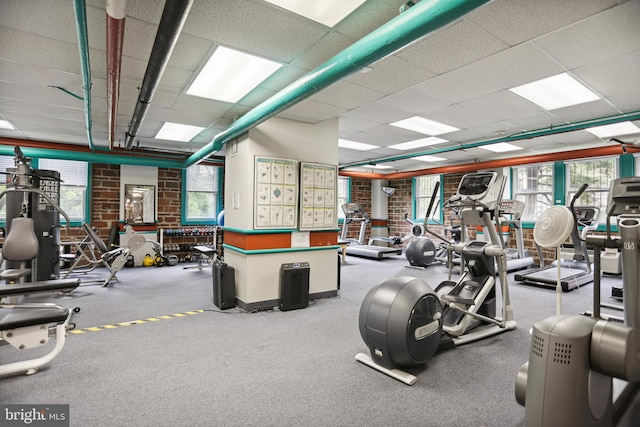 exercise room with brick wall, a drop ceiling, and a healthy amount of sunlight