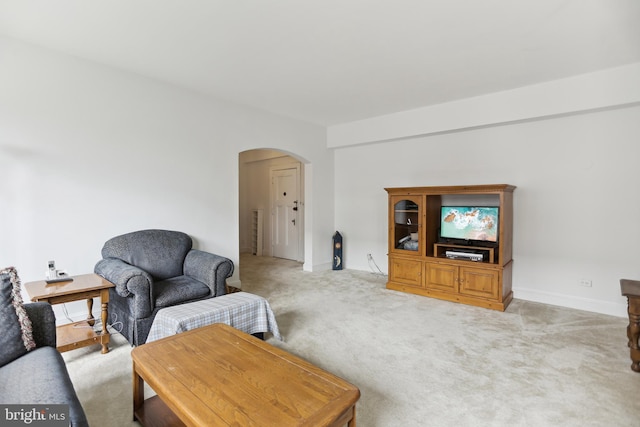 living area with arched walkways, light carpet, and baseboards