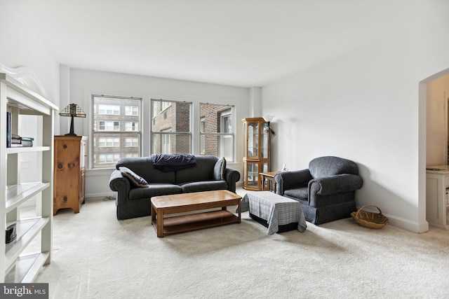 living area featuring baseboards, arched walkways, and light colored carpet