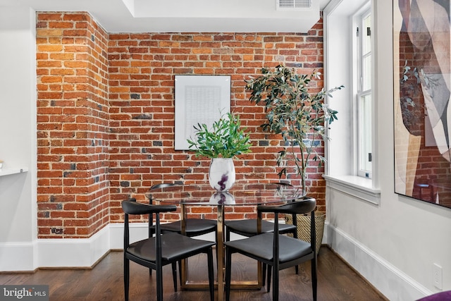 dining space with visible vents, wood finished floors, baseboards, and brick wall