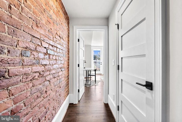 hallway featuring dark wood-style floors, baseboards, and brick wall