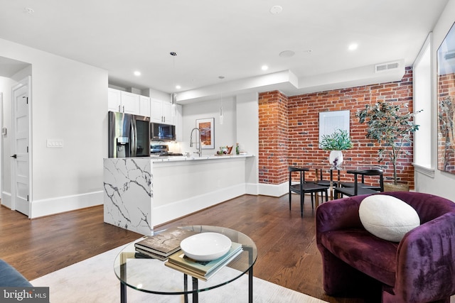 living room featuring visible vents, recessed lighting, brick wall, baseboards, and dark wood-style flooring