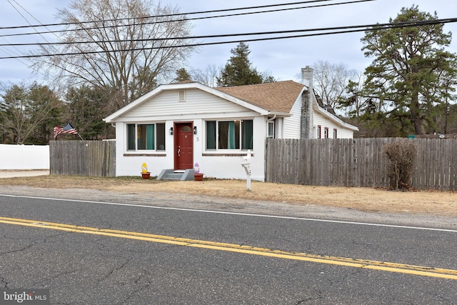 bungalow-style home with a chimney, uncovered parking, fence, and roof with shingles