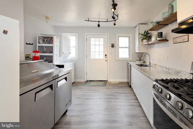 kitchen with open shelves, stacked washer and dryer, white cabinetry, a sink, and stainless steel gas range oven