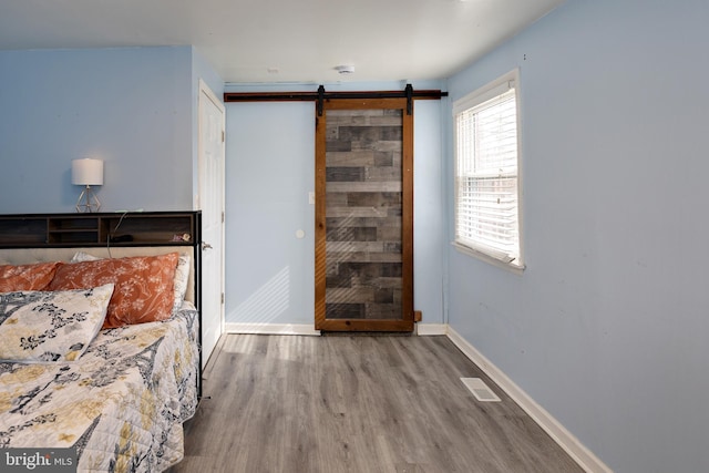 unfurnished bedroom with baseboards, a barn door, visible vents, and wood finished floors