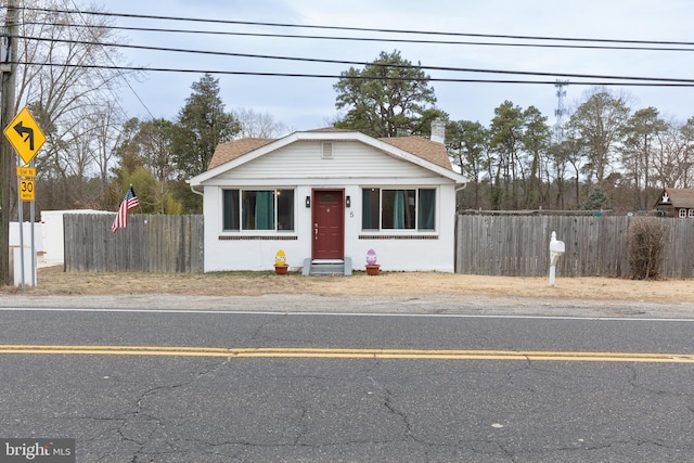 bungalow-style home with uncovered parking, a shingled roof, and fence