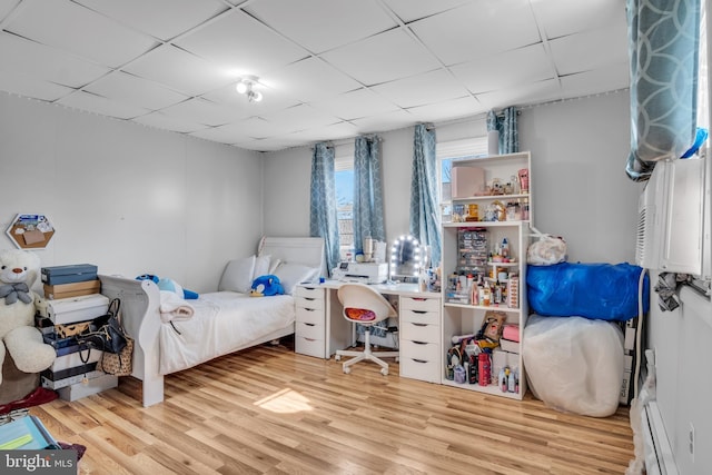 bedroom featuring a baseboard radiator, a drop ceiling, and wood finished floors