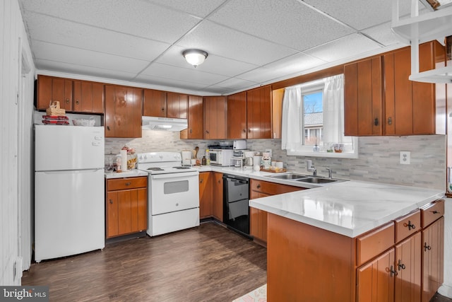 kitchen featuring light countertops, a sink, a peninsula, white appliances, and under cabinet range hood