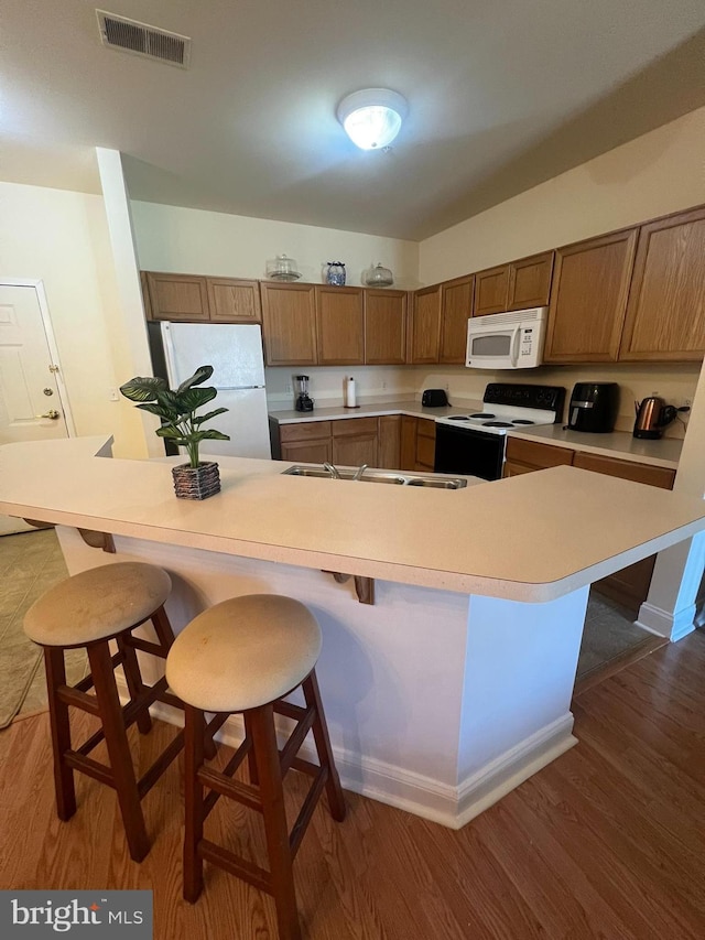 kitchen featuring white appliances, a breakfast bar area, visible vents, and wood finished floors