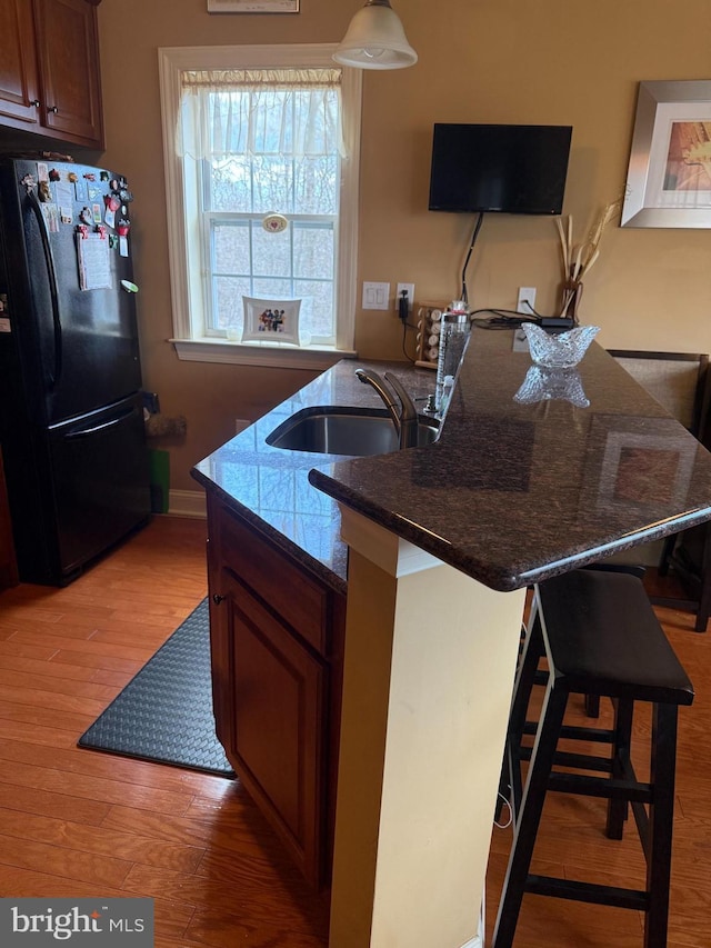 kitchen featuring dark countertops, light wood-style flooring, a kitchen breakfast bar, freestanding refrigerator, and a sink