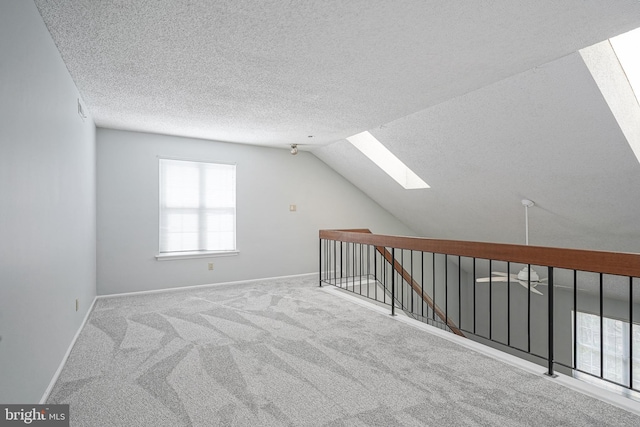 bonus room with carpet floors, vaulted ceiling with skylight, a textured ceiling, and baseboards