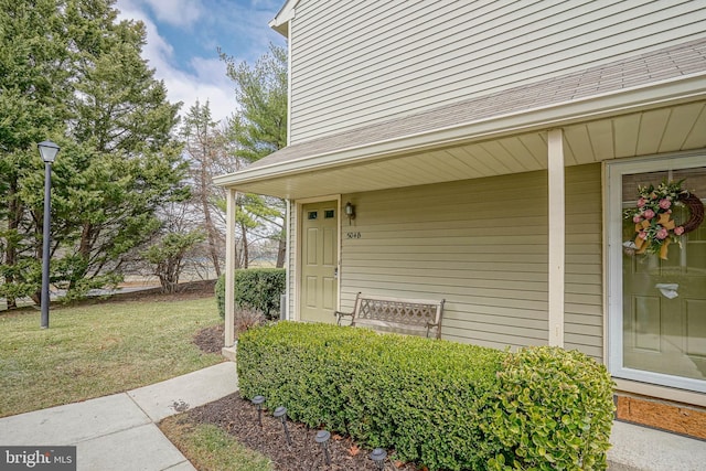 property entrance with roof with shingles and a yard